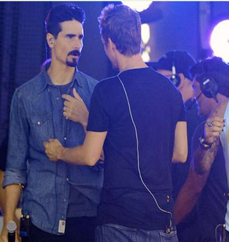 La imagen muestra a Kevin Richardson con cara de enojado y a su compañero tomándolo de la camisa
